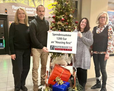 4 Personen stehen vor einem Weihnachtsbaum mit einem Plakat auf dem die Spendsumme 1200 Euro steht